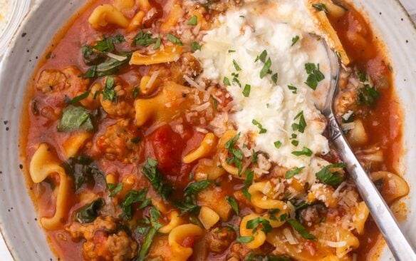 Overhead view of a full bowl of lasagna soup with a spoon in it.