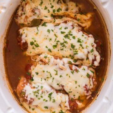 overhead image of four salsa chicken breasts in slow cooker with mozzarella and parsley