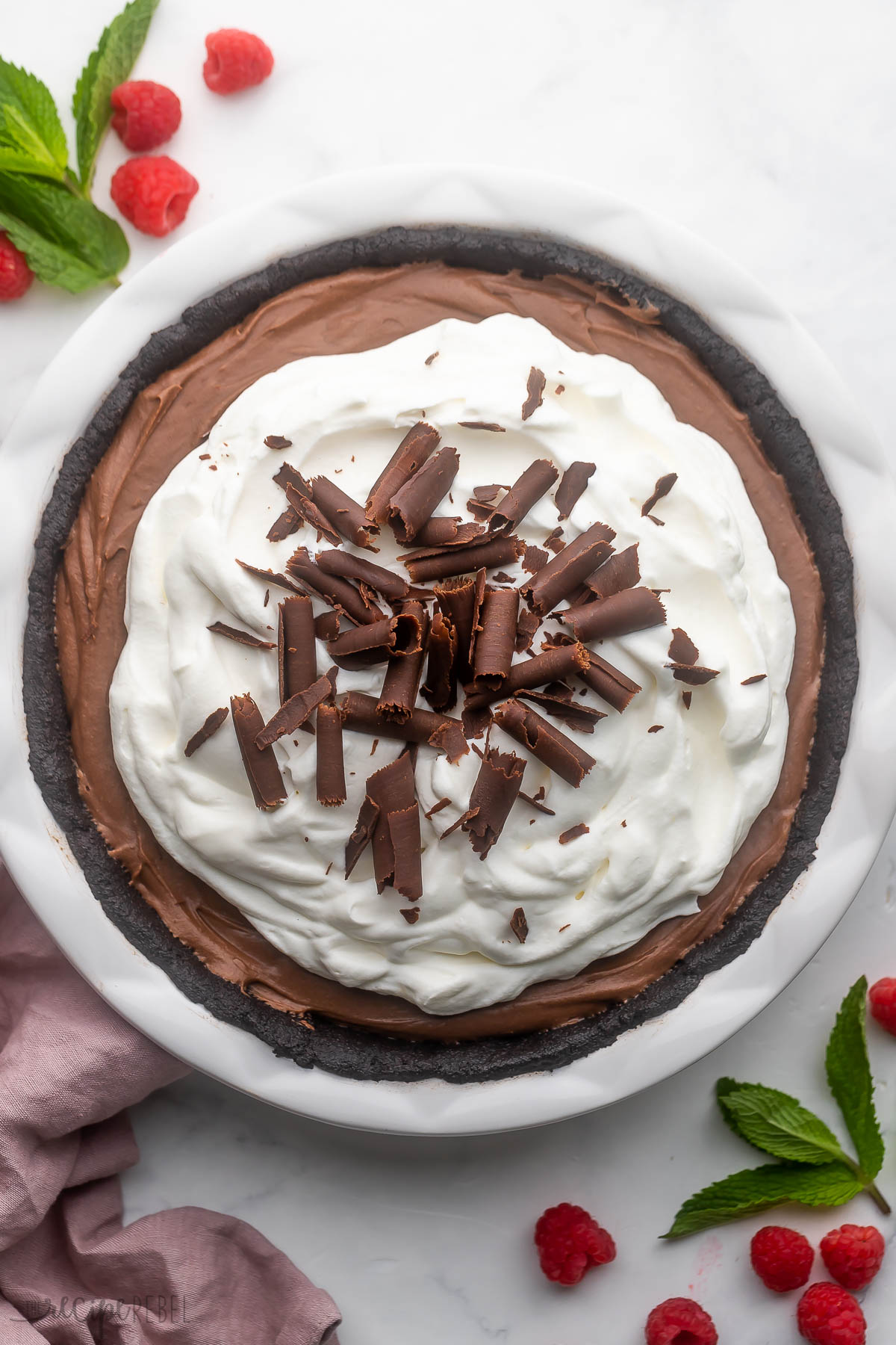 overhead view of a full french silk pie with chocolate curls on top with raspberries and mint leaves beside.