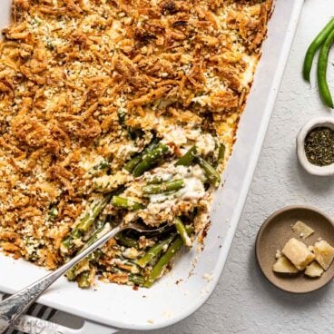 close up a spoon scooping green bean casserole out of white baking dish.