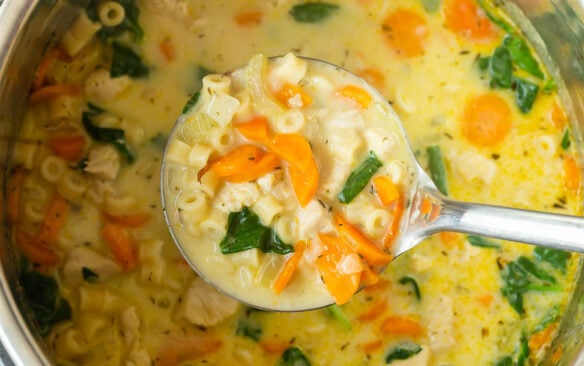 metal ladle scooping chicken noodle soup from instant pot.