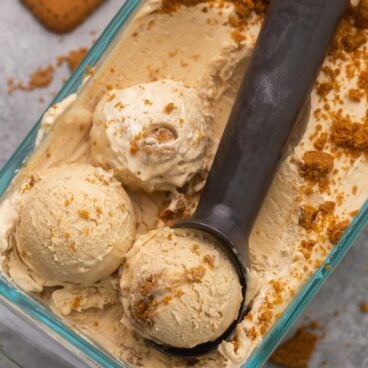 Top view of no churn Biscoff ice cream in a glass dish with an ice cream scoop in it.