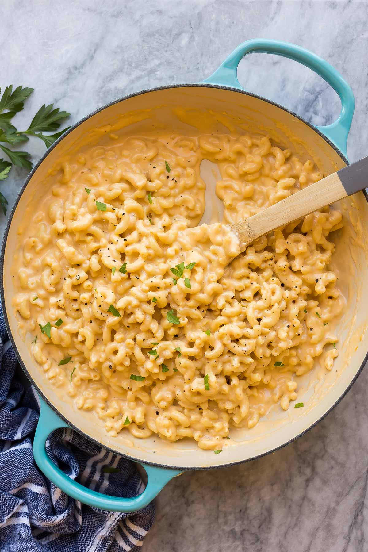 blue skillet of mac and cheese on marble background with wooden spoon