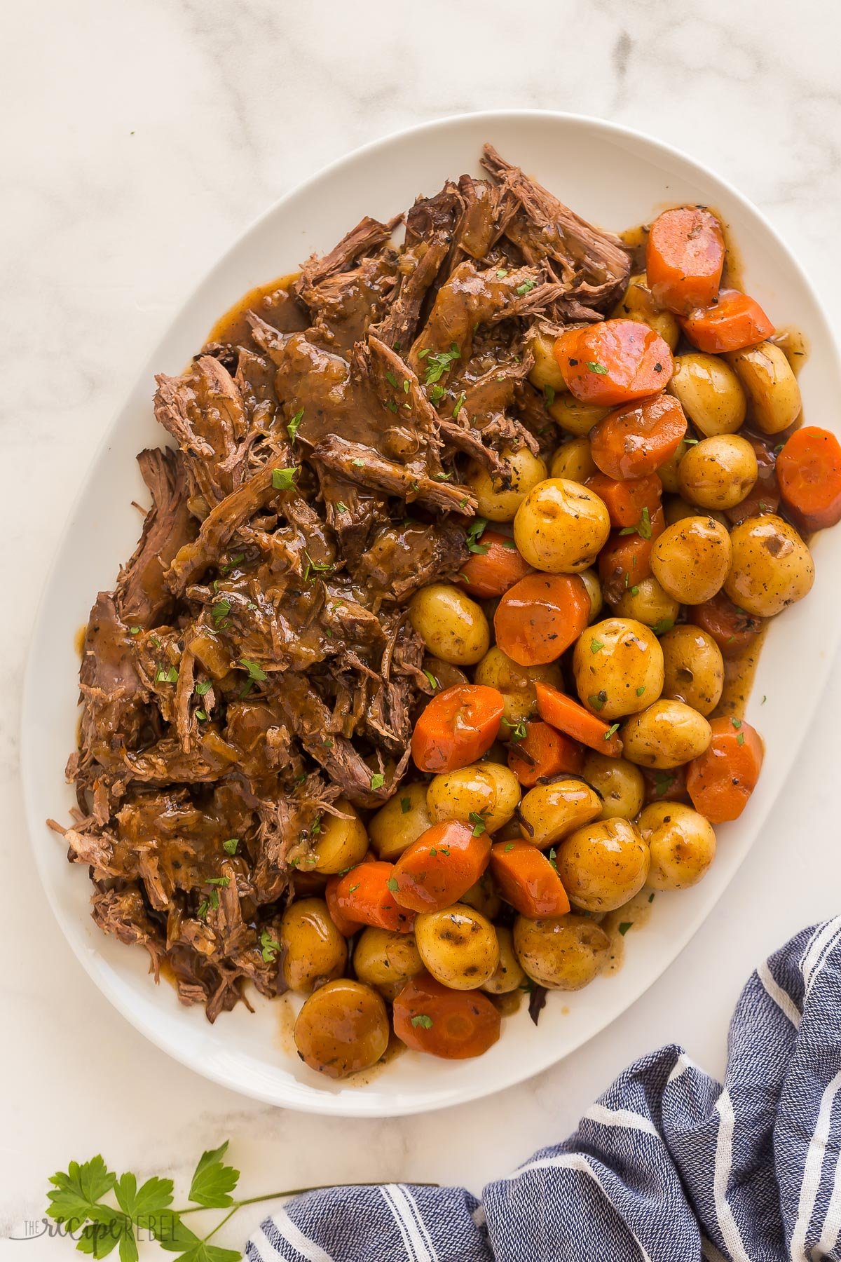 overhead image of slow cooker pot roast on white platter with a blue towel
