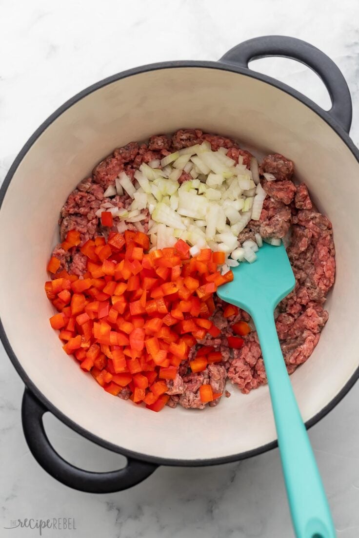 large pot with uncooked beef, onions, and red peppers.